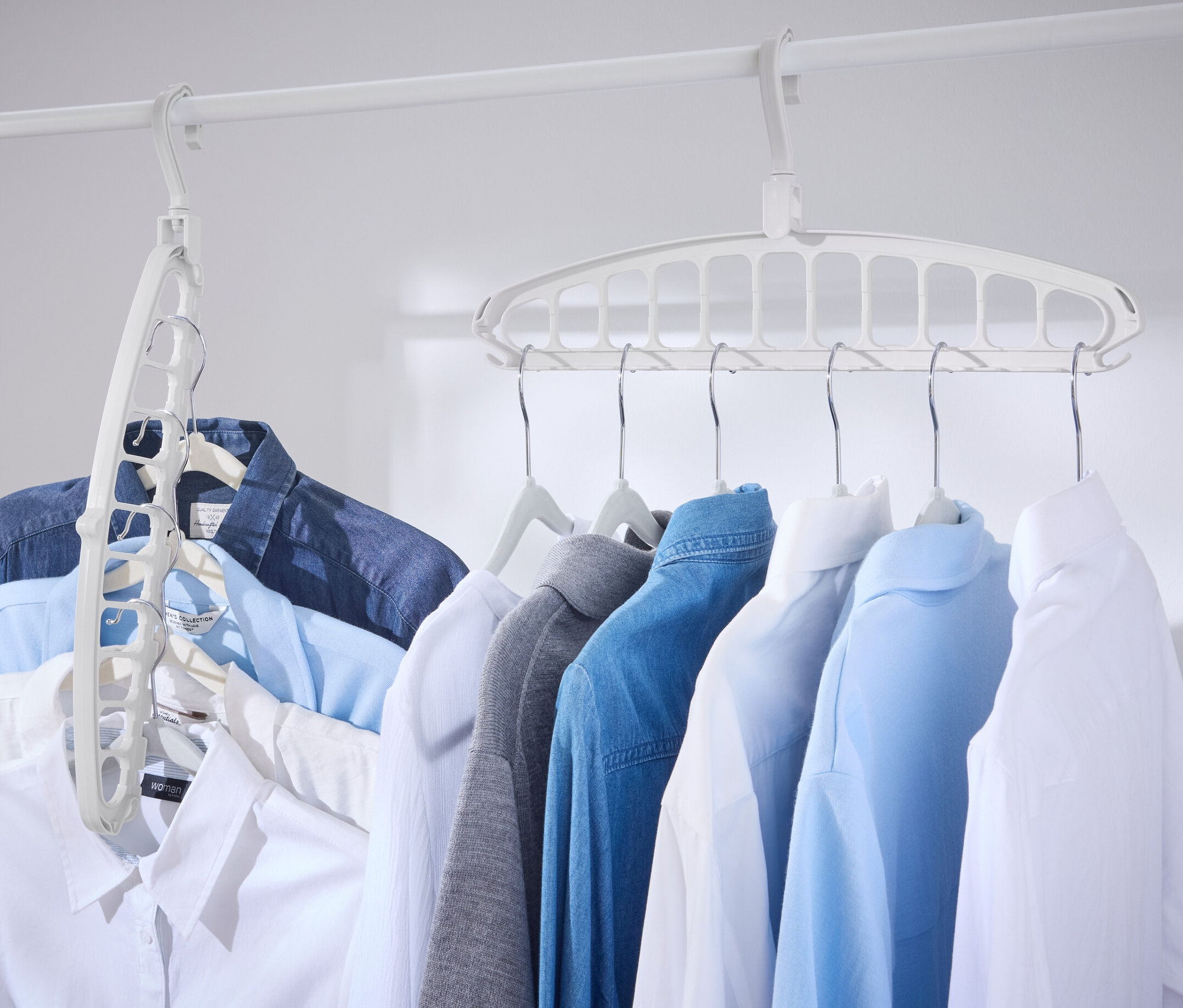 Niekoľko košieľ visí na bielej tyči s multifunkčnými vešiakmi, 2 ks.