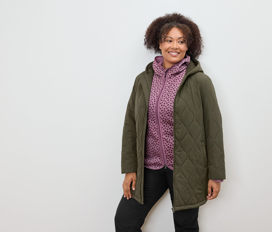 Žena v olivovom prešívanom kabáte a fialovej vzorovanej mikine s kapucňou.