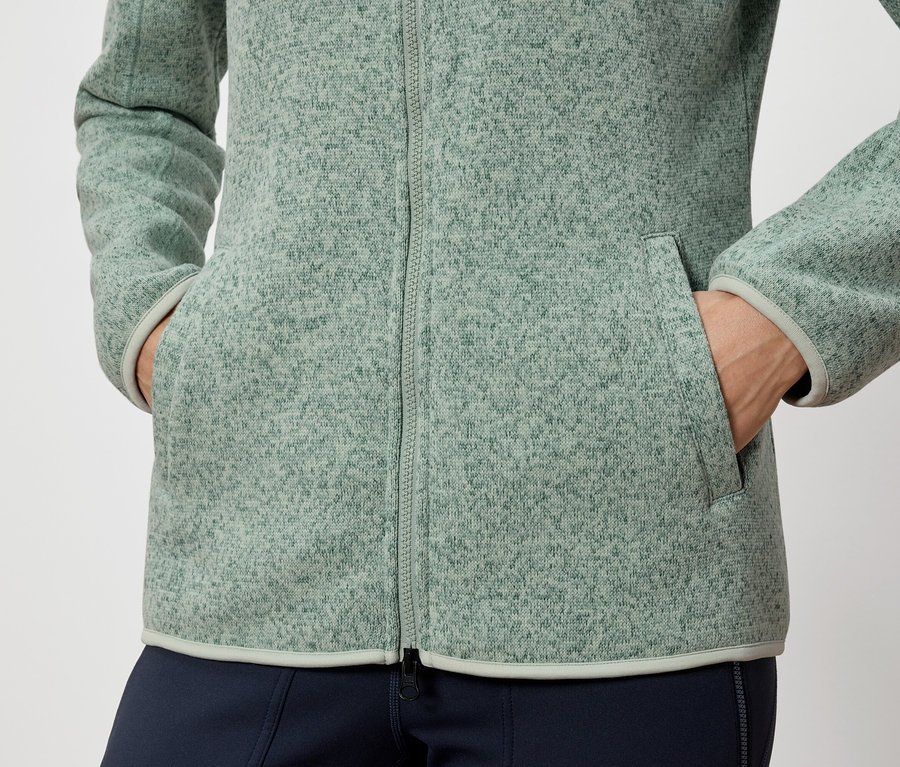Osoba má ruky vo vreckách zelenej fleecovej bundy.