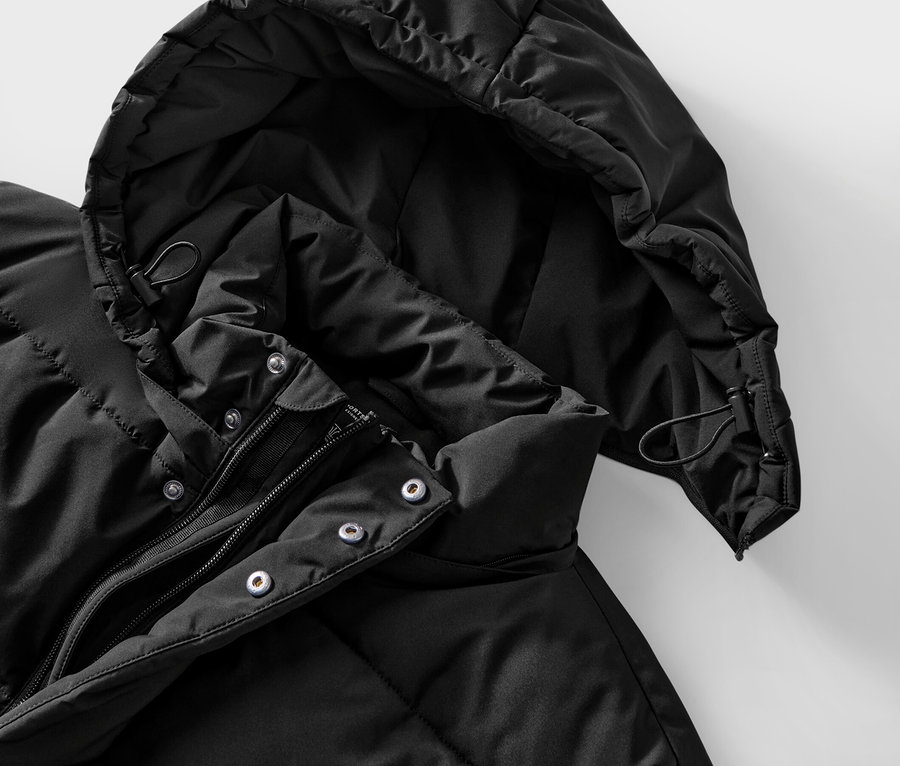 Detail čiernej prešívanej bundy s kapucňou a zipsom.
