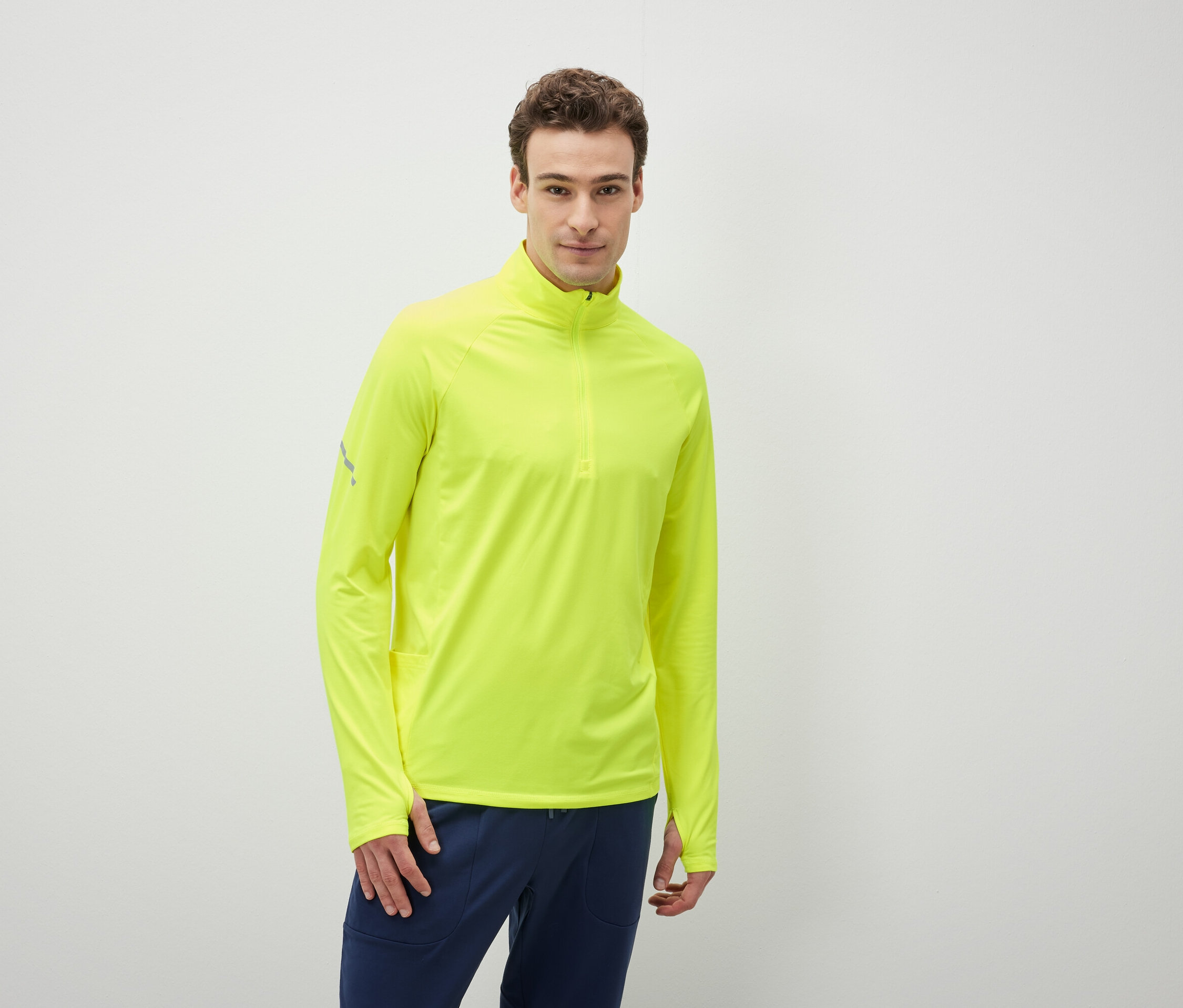 Muž má na sebe neónovo žlté tričko s dlhým rukávom a tmavomodré nohavice.