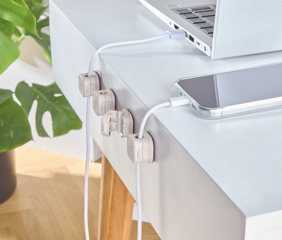 Strieborný notebook a telefón sa nabíjajú na bielom stole s drevenými držiakmi káblov.