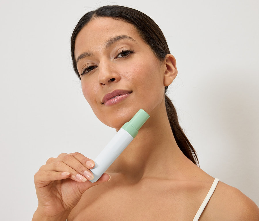 Žena drží bielo-zelenú fľašu pred tvárou.