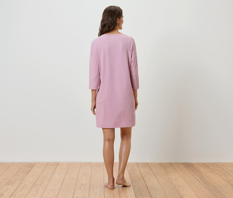 Žena stojí chrbtom k fotoaparátu a má na sebe ružové šaty s trojštvrťovými rukávmi.