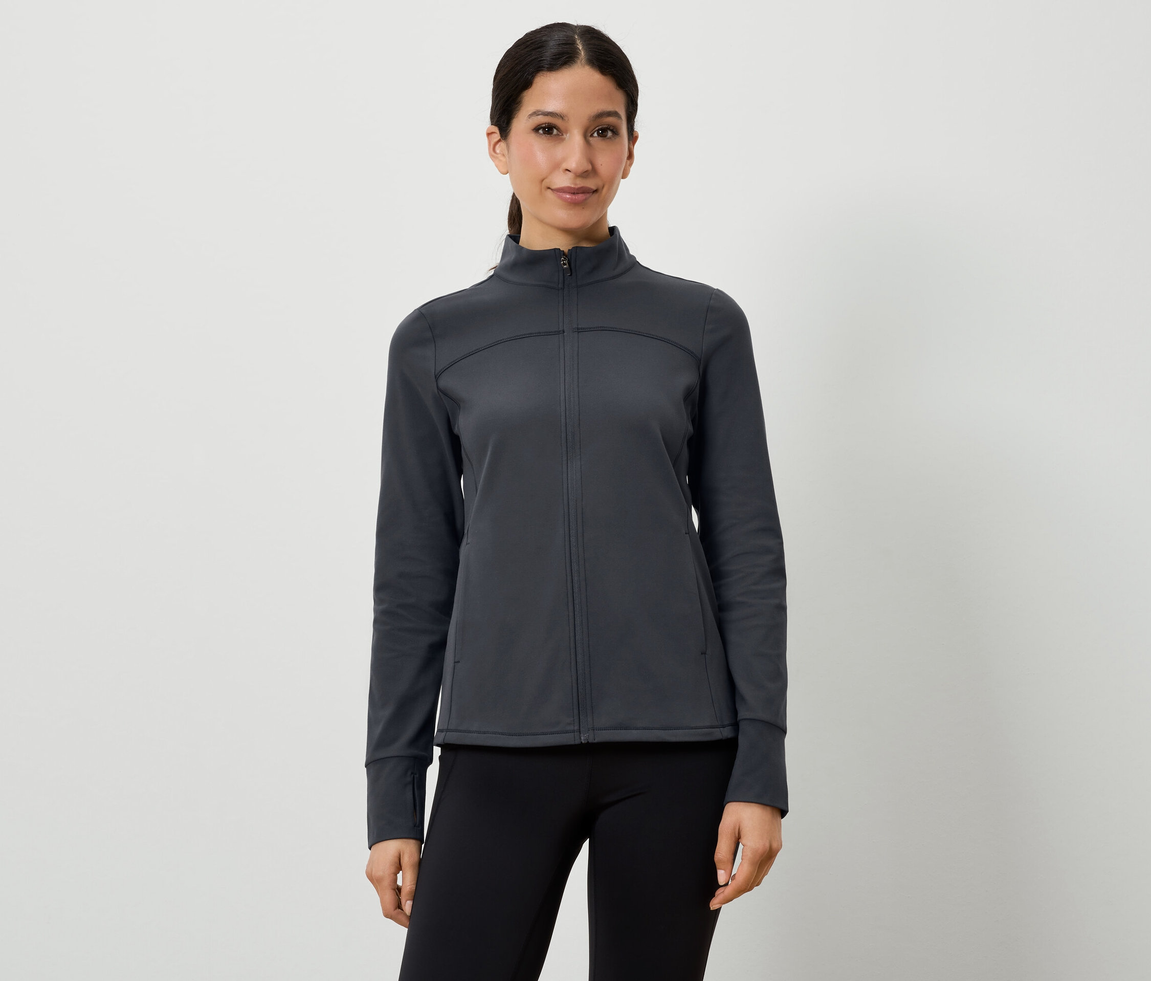 Žena má na sebe tmavosivú športovú bundu a čierne legíny.