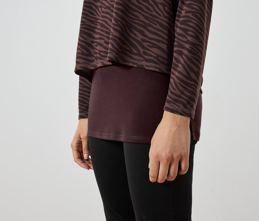 Detail ženy nosiacej hnedo-čiernu zebrovanú tuniku, vínový top a čierne legíny.