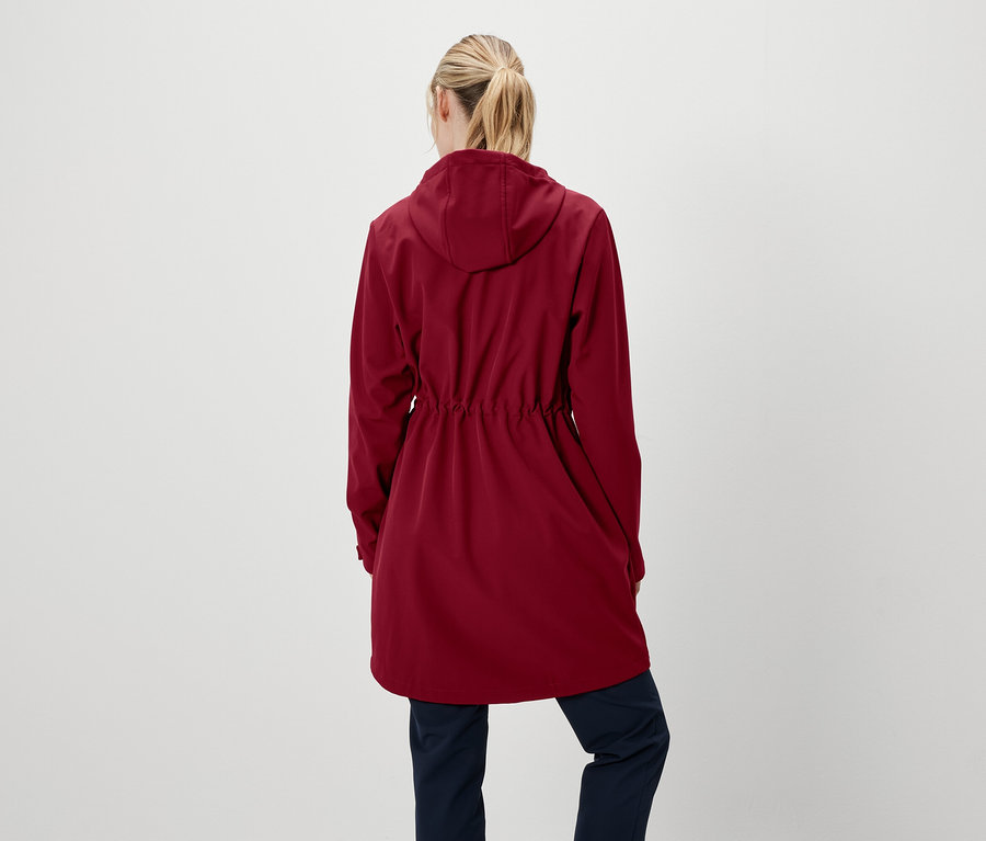 Žena chrbtom k fotoaparátu má na sebe červenú bundu s kapucňou a tmavomodré nohavice.