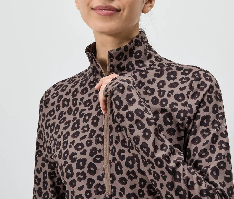 Žena v hnedom tope s dlhým rukávom s leopardím vzorom, ktorá si rozopína zips.