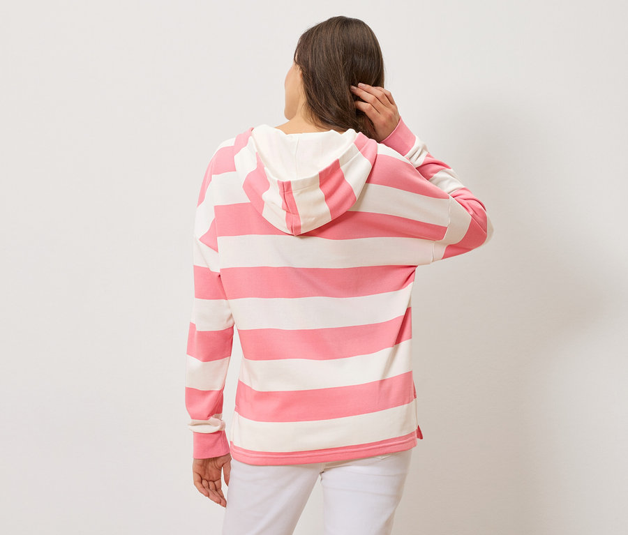 Žena zozadu, má na sebe ružovo-bielu pruhovanú mikinu s kapucňou a biele nohavice.