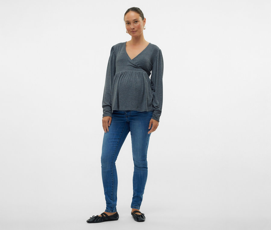 Žena v šedej zavinovacej blúzke a skinny džínsoch MAMALICIOUS »MLMILA« pózuje na bielom pozadí.