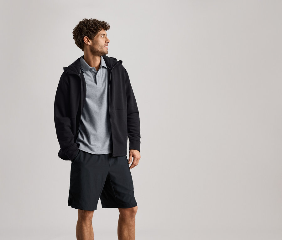 Muž má na sebe čiernu mikinu so zipsom cez sivé polotričko a čierne šortky.