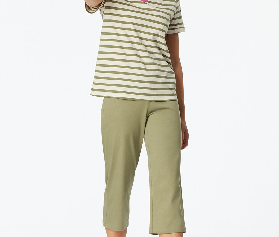 Žena stojí naboso a má na sebe pruhované tričko s výstrihom do V a zelené capri nohavice.