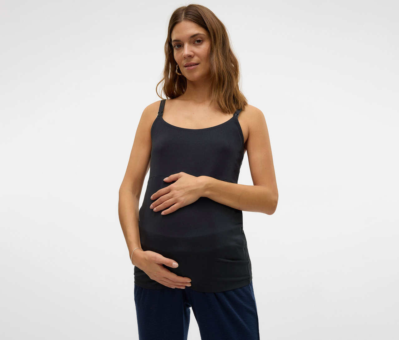 Tehotná žena s rukami na bruchu má na sebe tielko s tenkými ramienkami MAMALICIOUS »MLKERRIE«.