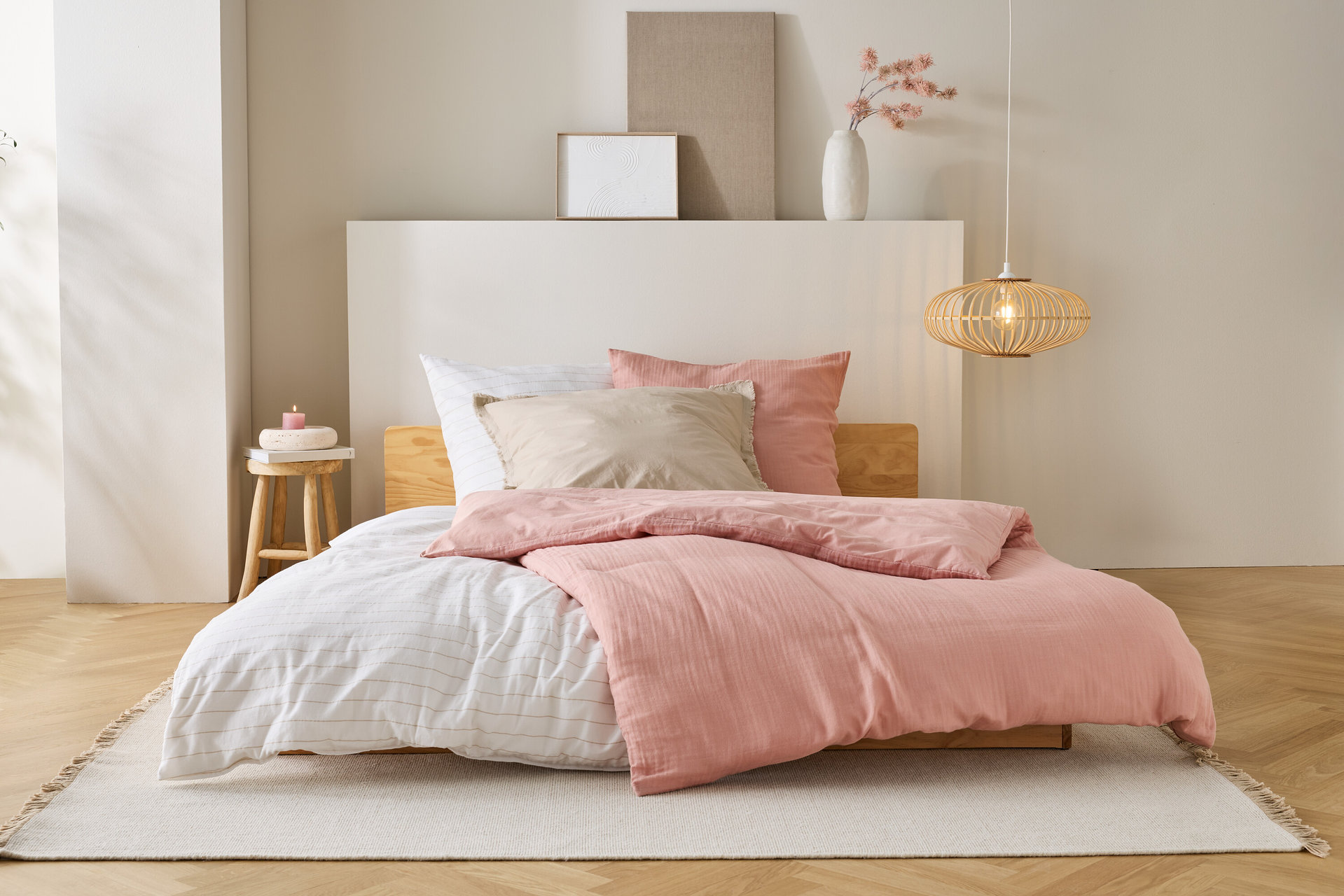 Posteľ s ružovou prikrývkou, bielymi plachtami a béžovými vankúšmi stojí na koberci v spálni.