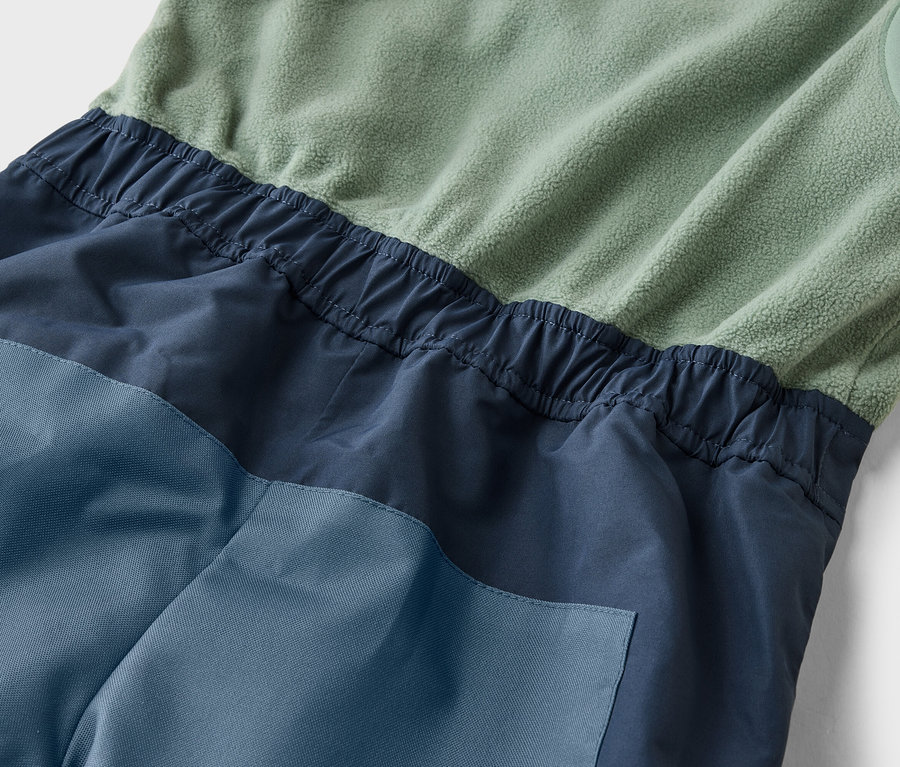 Detail záberu overalu bez rukávov v zelenej, námorníckej a modrej farbe s elastickým pásom.