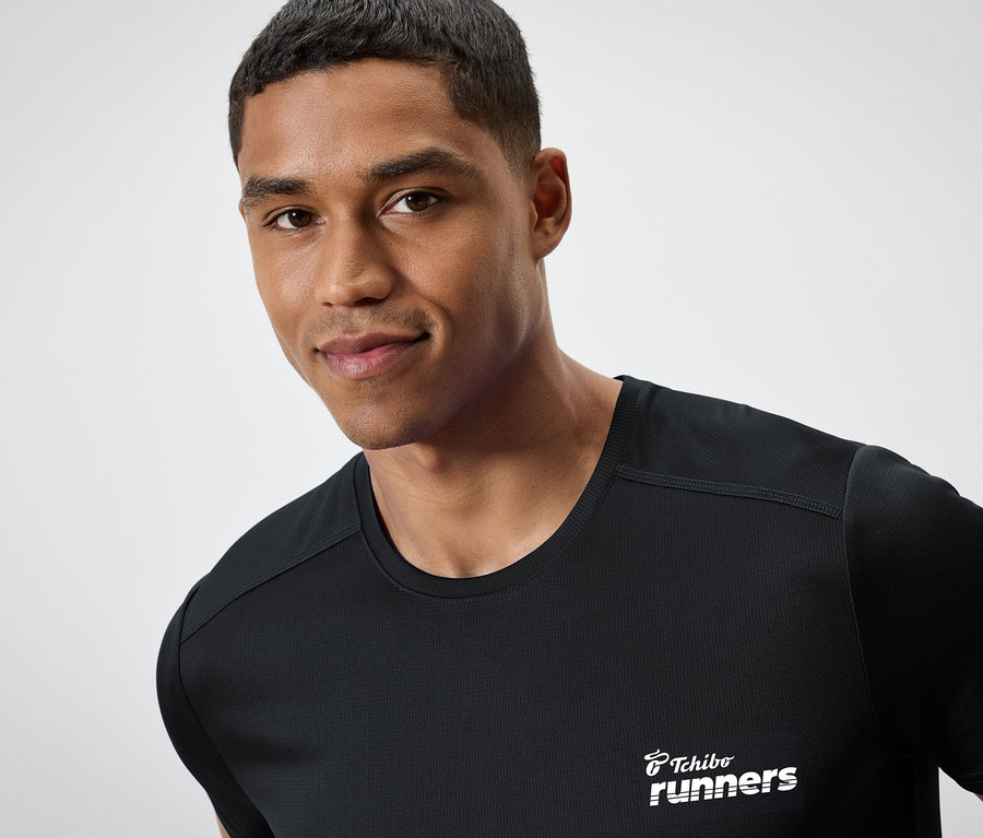 Muž s tmavou pokožkou má na sebe čierne tričko s nápisom "Tchibo runners".