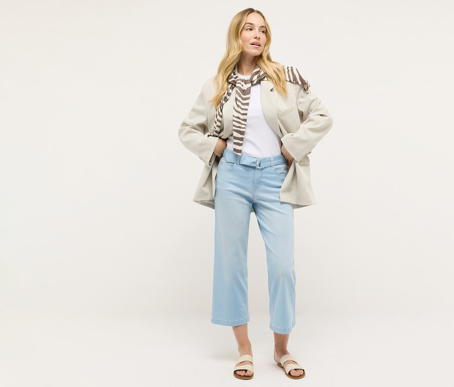 Žena stojí a má na sebe Angels Denim »Linn City« skrátený strih, vybielené modré, biele tričko, sako a šál.