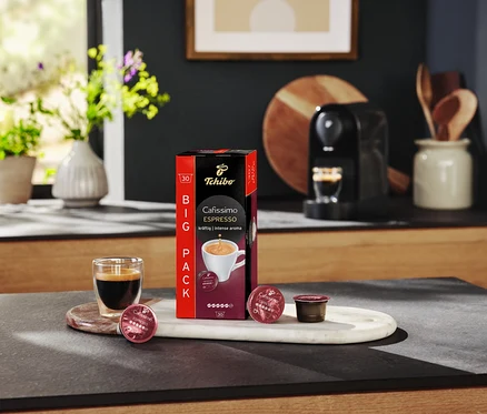 Espresso sklo stojí vedľa balenia Cafissimo Espresso a kapsúl na mramorovej tácke.