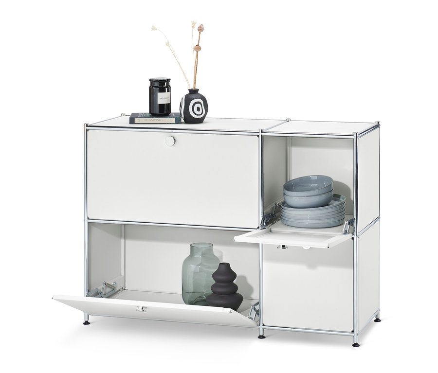 Biela odkladacia skrinka »CN3« so 4 výklopnými dvierkami. Na hornej strane skrinky váza a sviečka, vo vnútri skrinky taniere a misky.