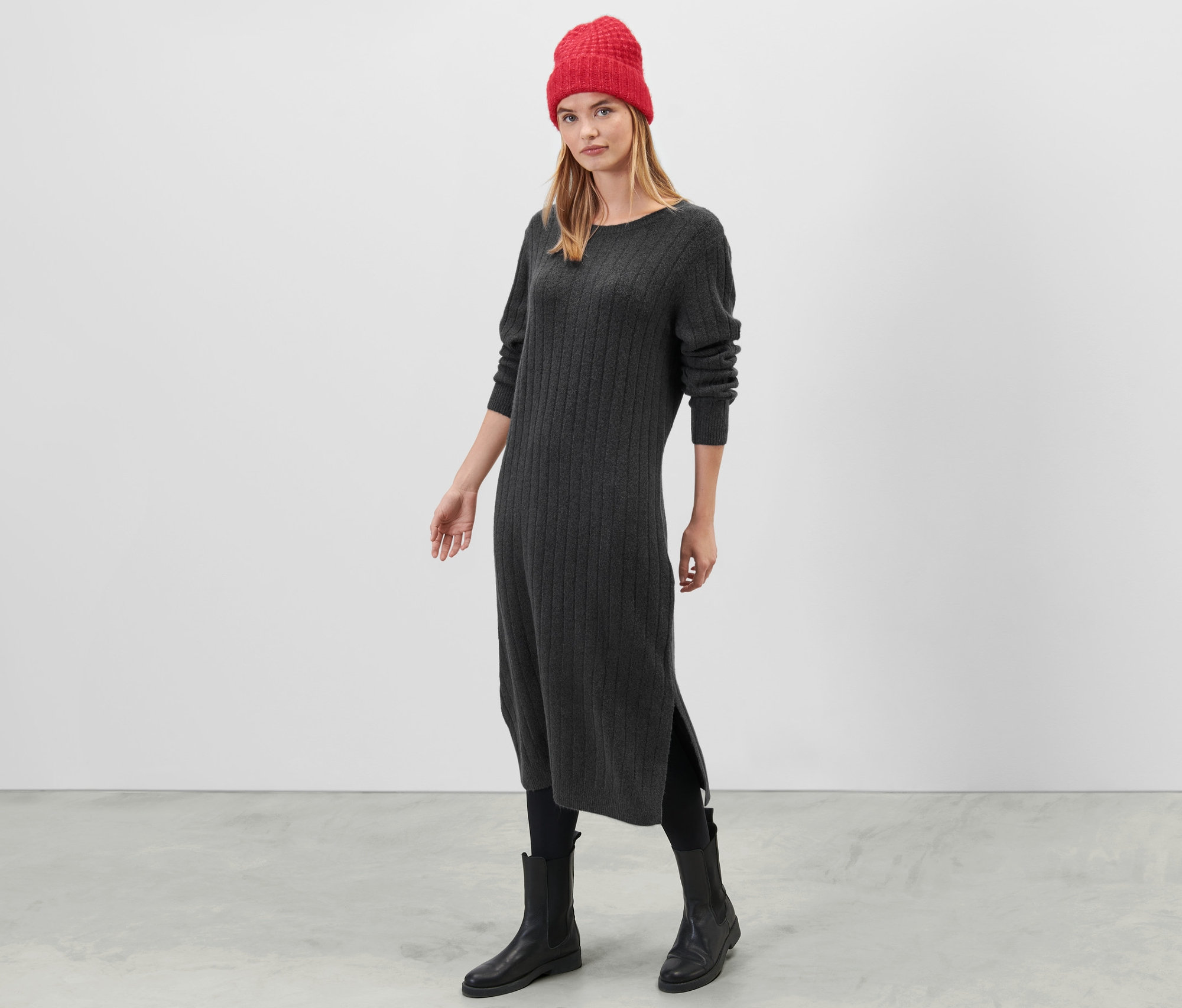 Žena stojí a má na sebe sivé šaty z rebrovaného úpletu.