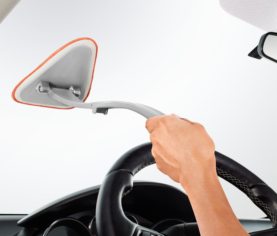 Ruka drží čistič autoskiel a čistí čelné sklo auta.