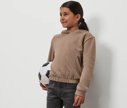 Dievča drží futbalovú loptu a má na sebe detskú mikinu s kapucňou.