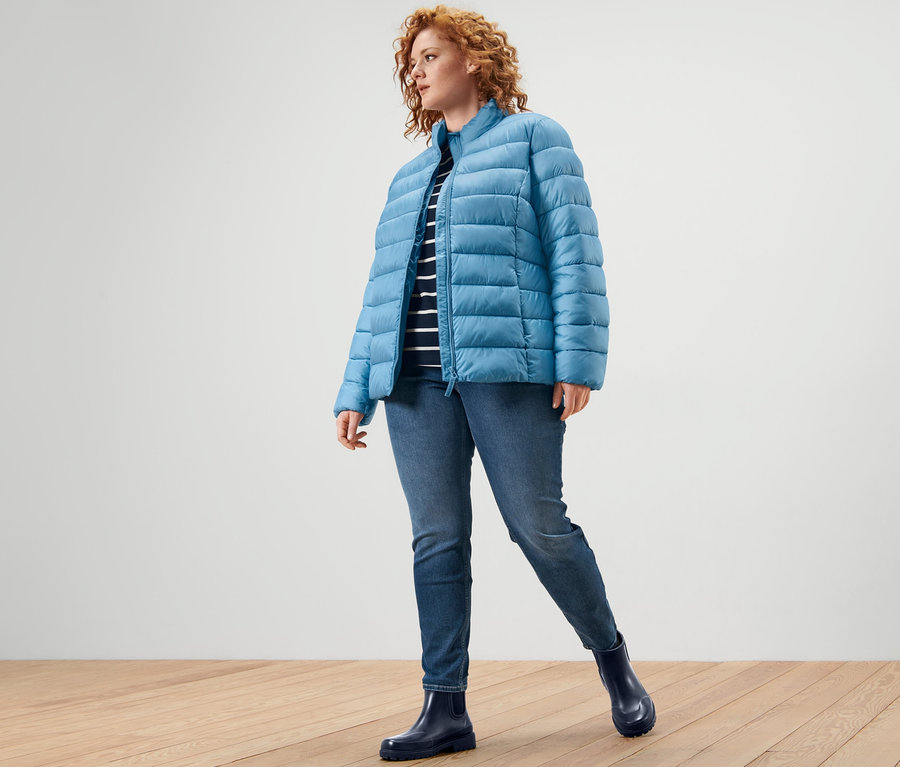 Žena má na sebe prešívanú bundu, prúžkované tričko s trojštvrťovými rukávmi a tregínsy »Fit Nelly«.