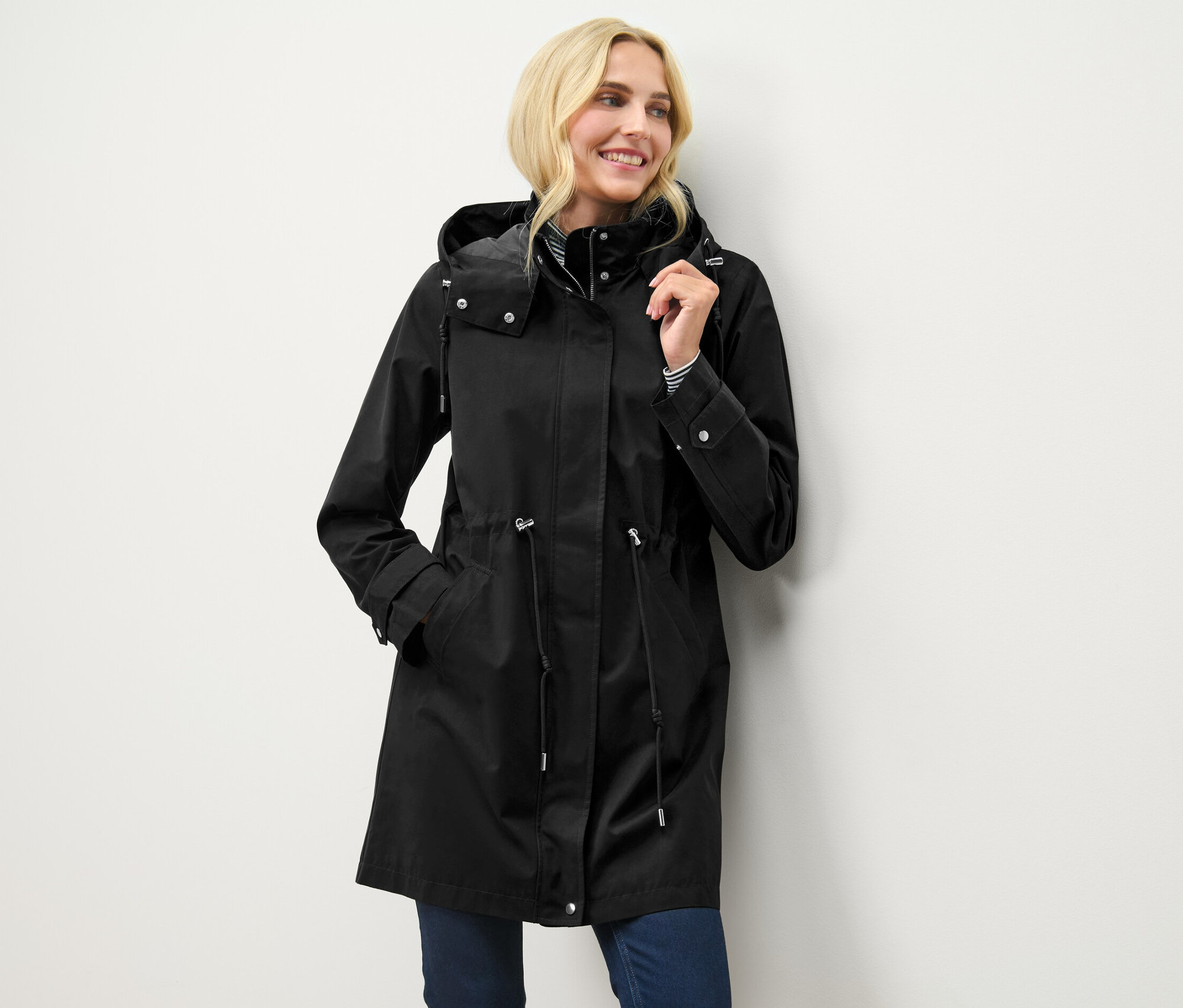 Blondína pózuje v čiernej parke s kapucňou.