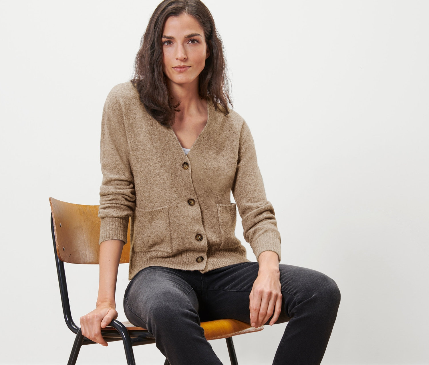 Žena sedí na stoličke a má na sebe pletený sveter s vlnou.