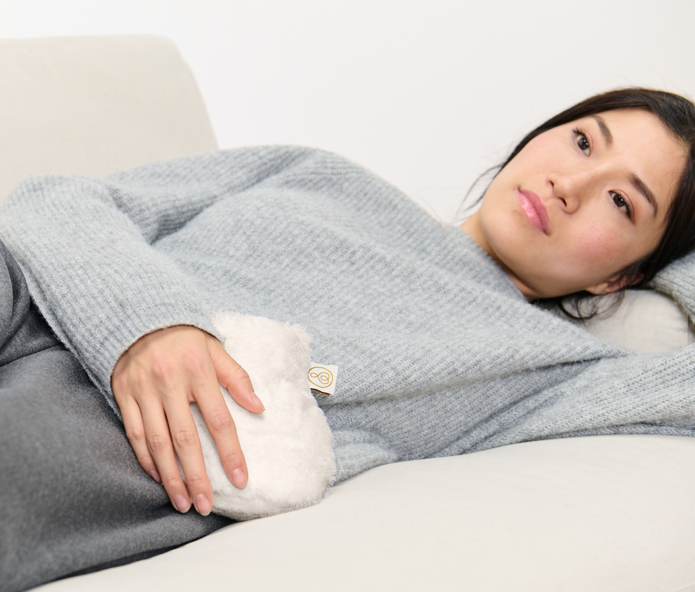 Žena leží na gauči a drží malý termofor.