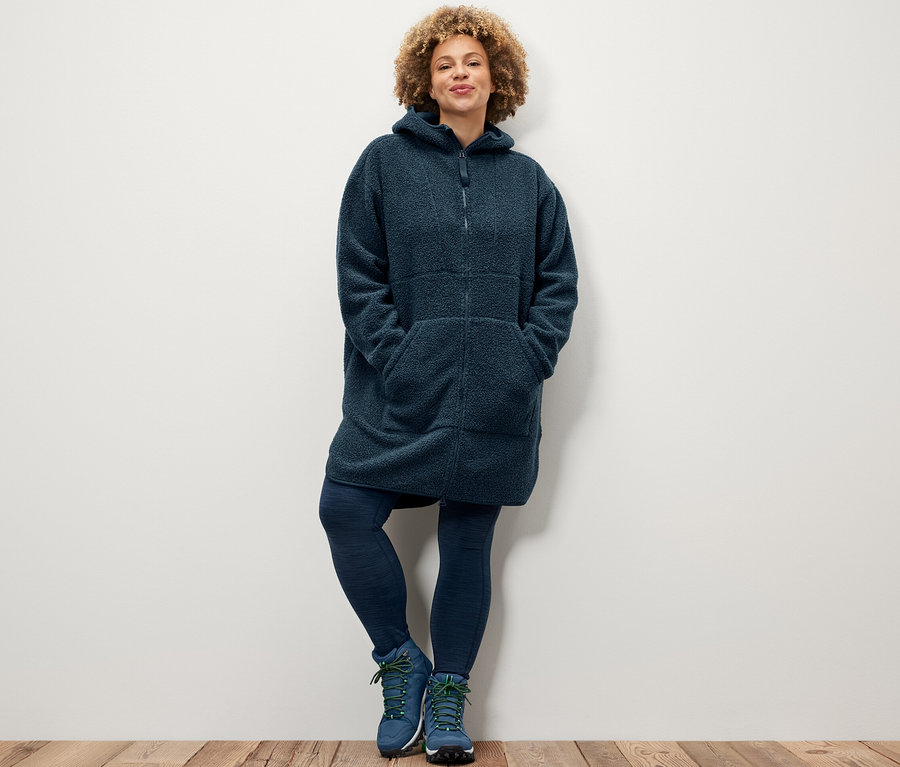 Žena pózuje v športových legínach a plyšovom kabáte v oversize štýle.