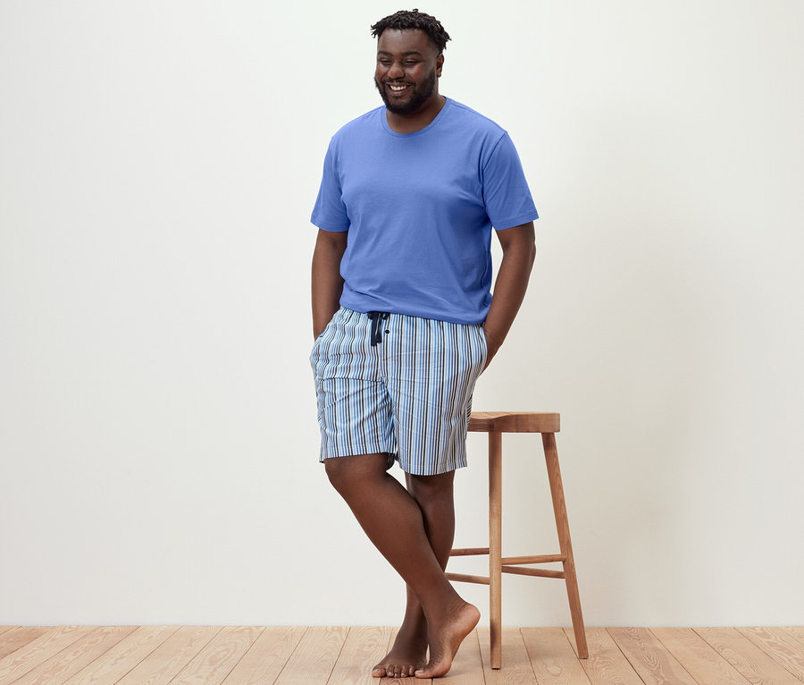 Muž sa opiera o stoličku a má na sebe krátke pyžamo.