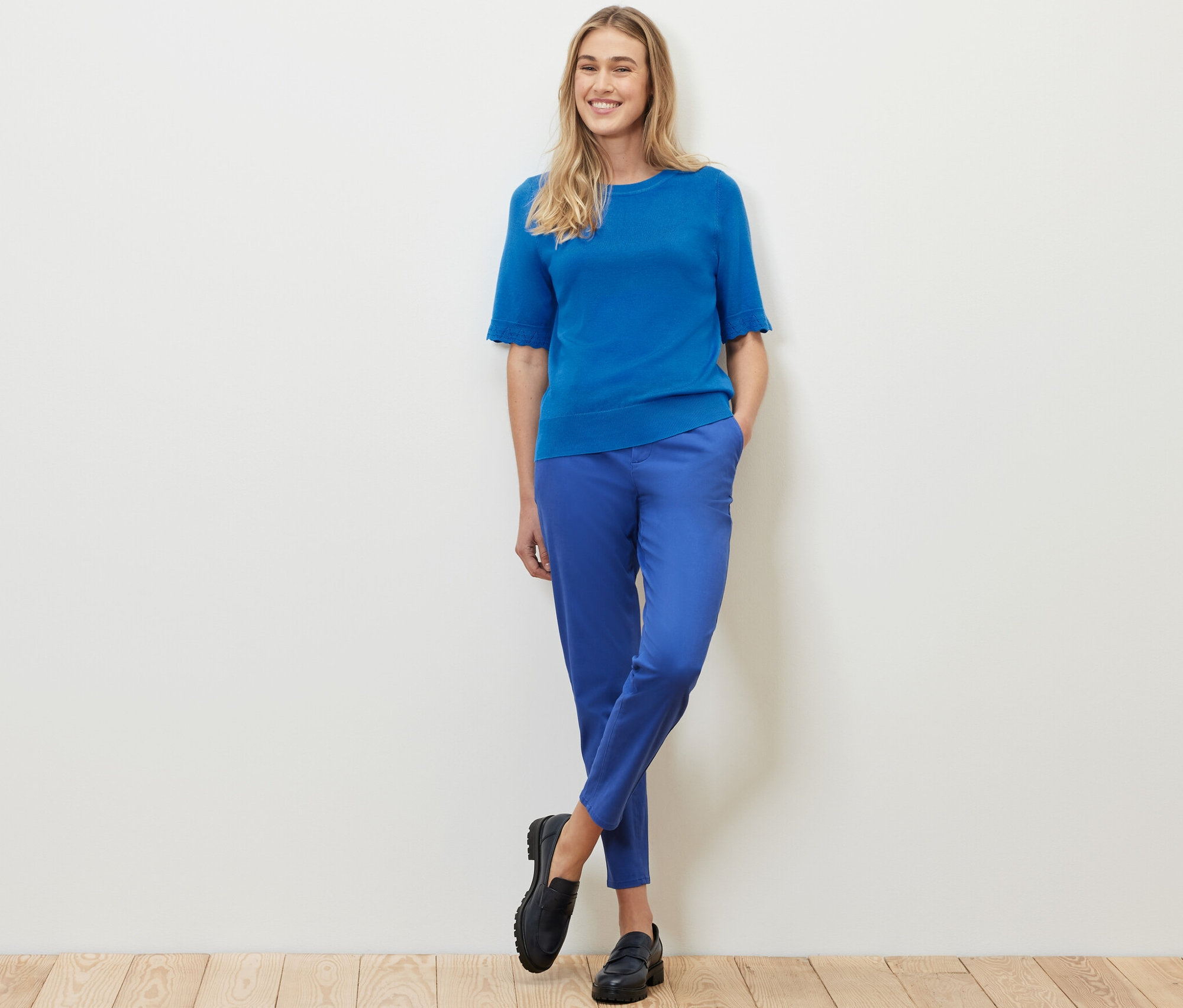 Žena stojí a pózuje v kobaltovomodrom pulóvri z jemného úpletu a modrých nohaviciach.