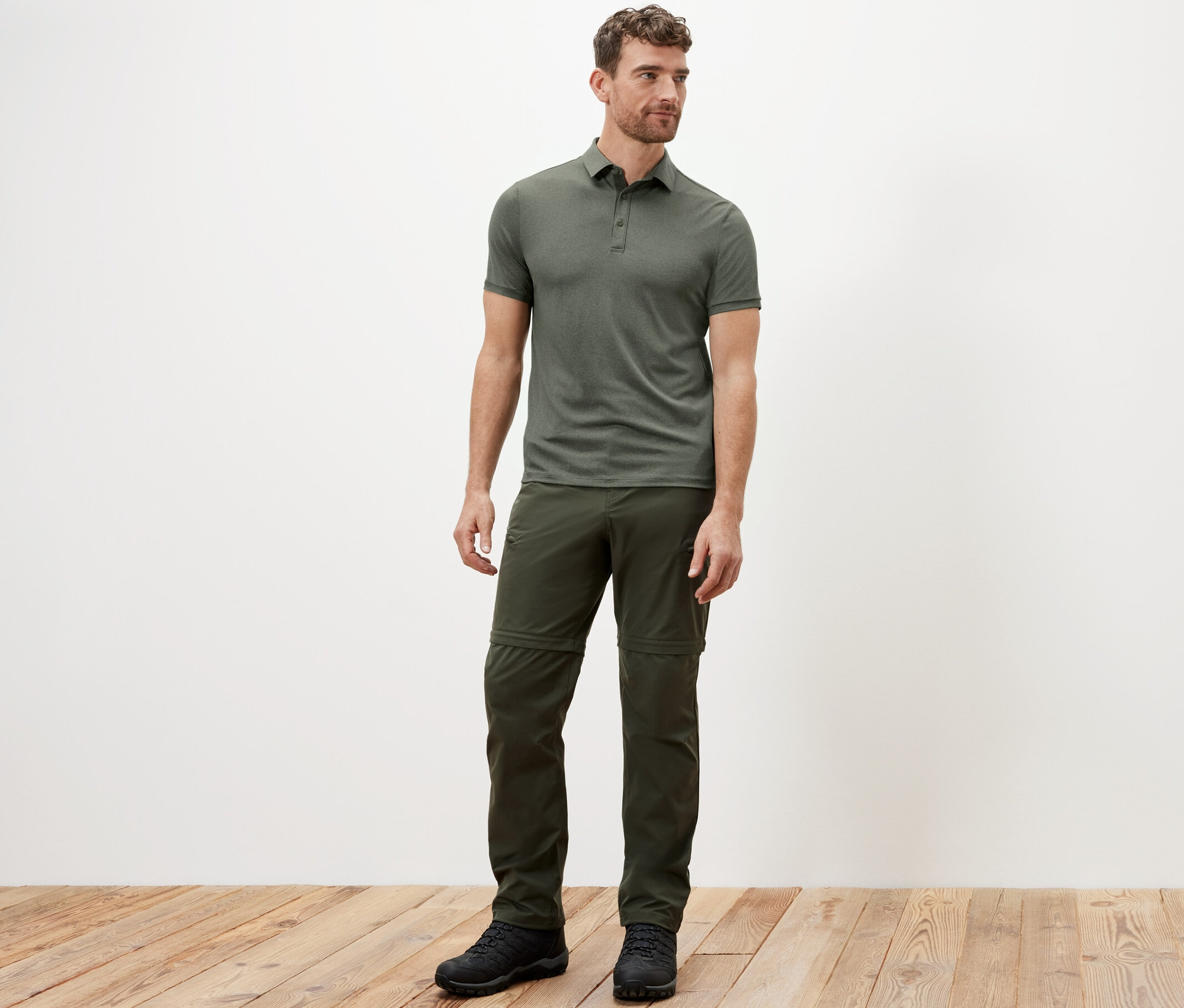 Muž stojí a má na sebe khaki funkčnú polokošeľu.