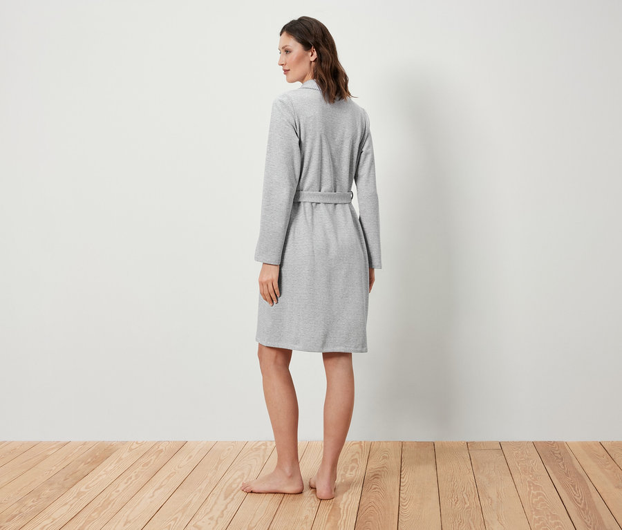 Žena stojí chrbtom a má na sebe sivý župan.