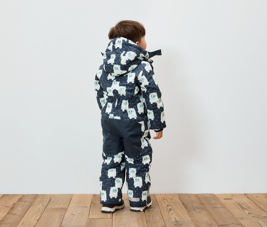 Chlapec stojí chrbtom a má na sebe modro-bielu kombinézu s kapucňou so vzorom snehuliakov.