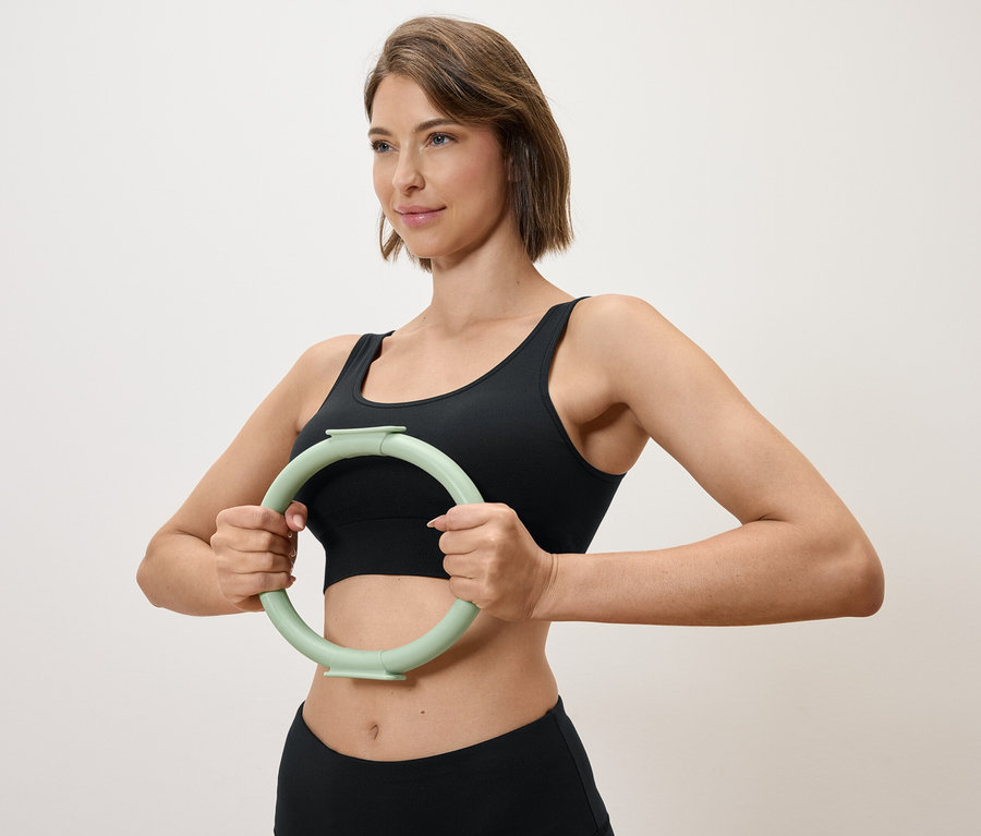 Žena drží svetlozelený kruh na cvičenie pred sebou, oblečená do čierneho športového topu a legín.