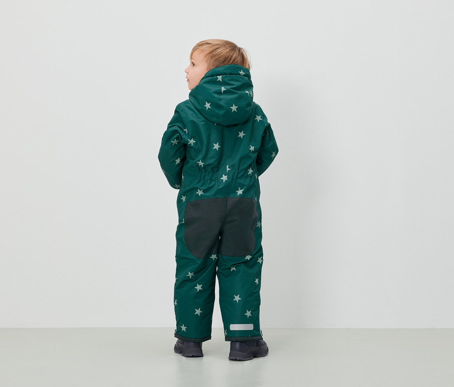 Chlapec v zelenej kombinéze so vzorom hviezd stojí chrbtom k fotoaparátu.