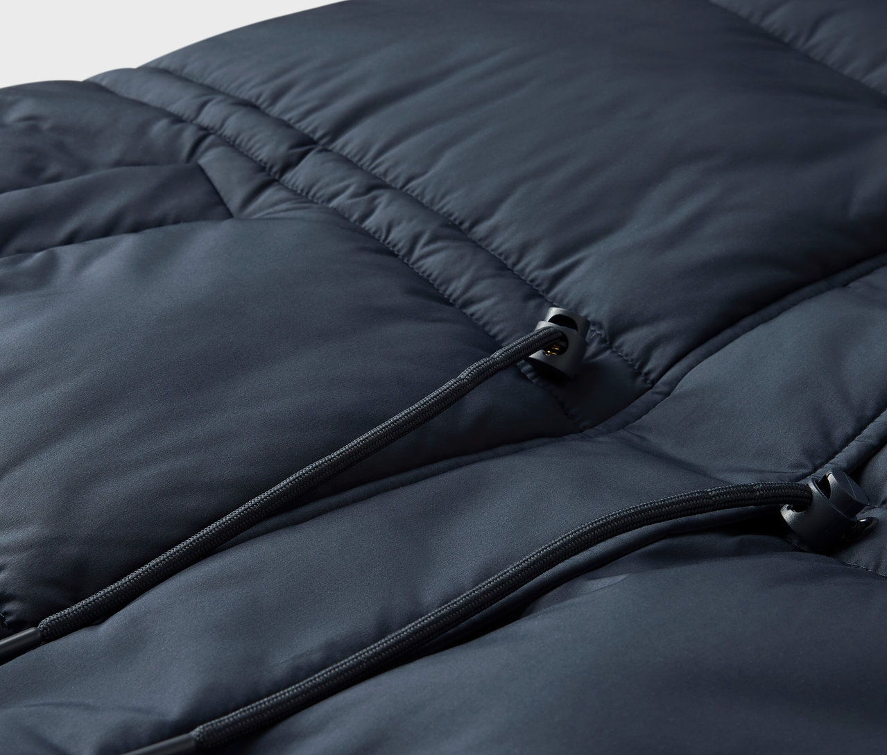 Detail prešívanej bundy tmavomodrej farby so sťahovacou šnúrkou.