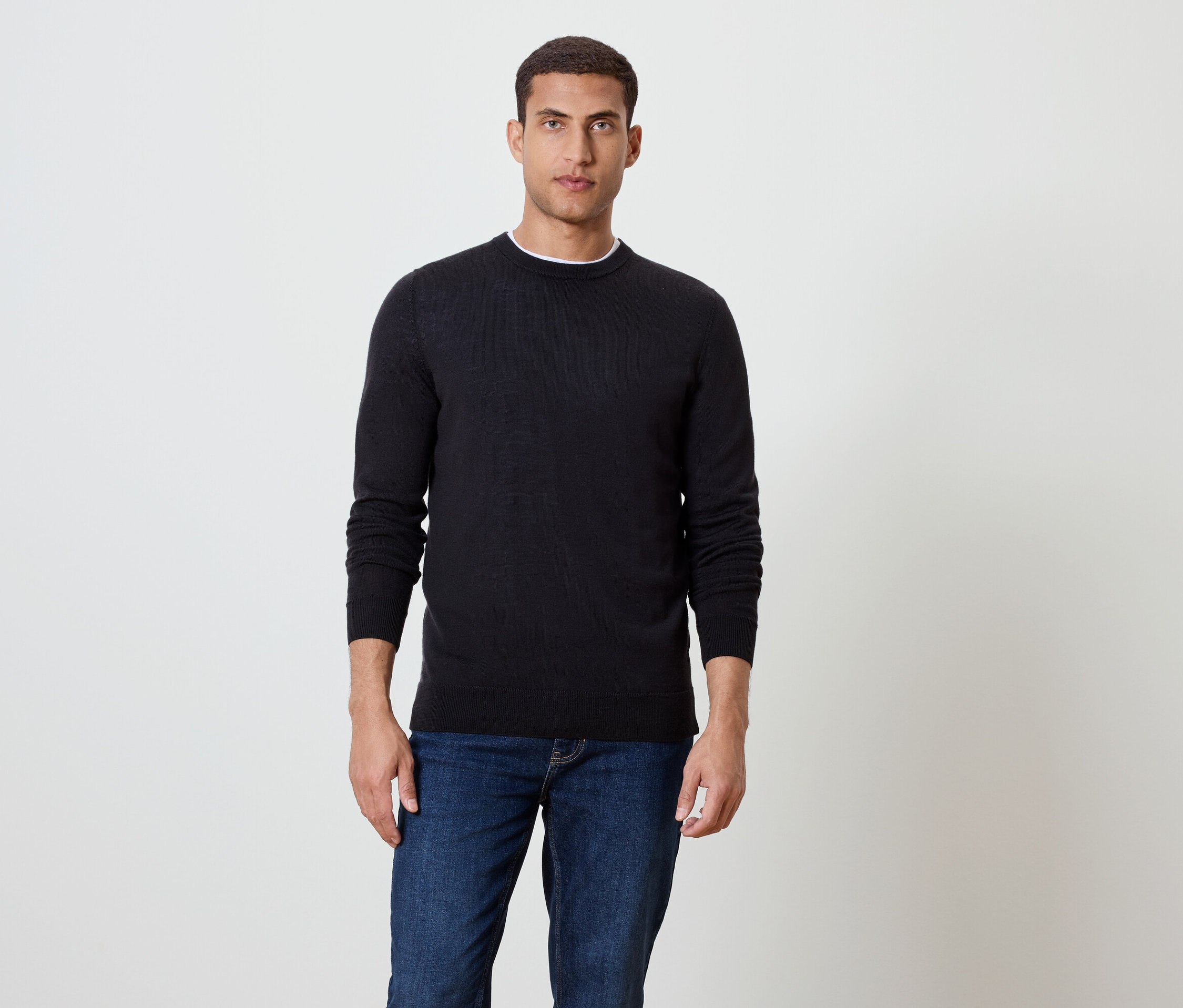 Muž stojí a má na sebe čierny sveter a modré džínsy.