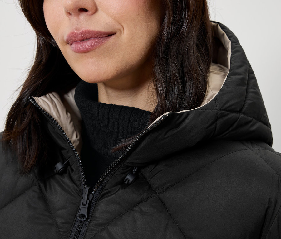 Detail dámy v čiernej prešívanej bunde s kapucňou a čiernym rolákom.