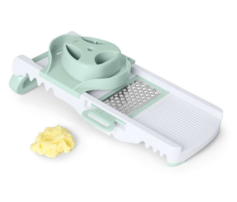 Biely a zelený mandolínový krájač s hromadou nakrájanej zeleniny.