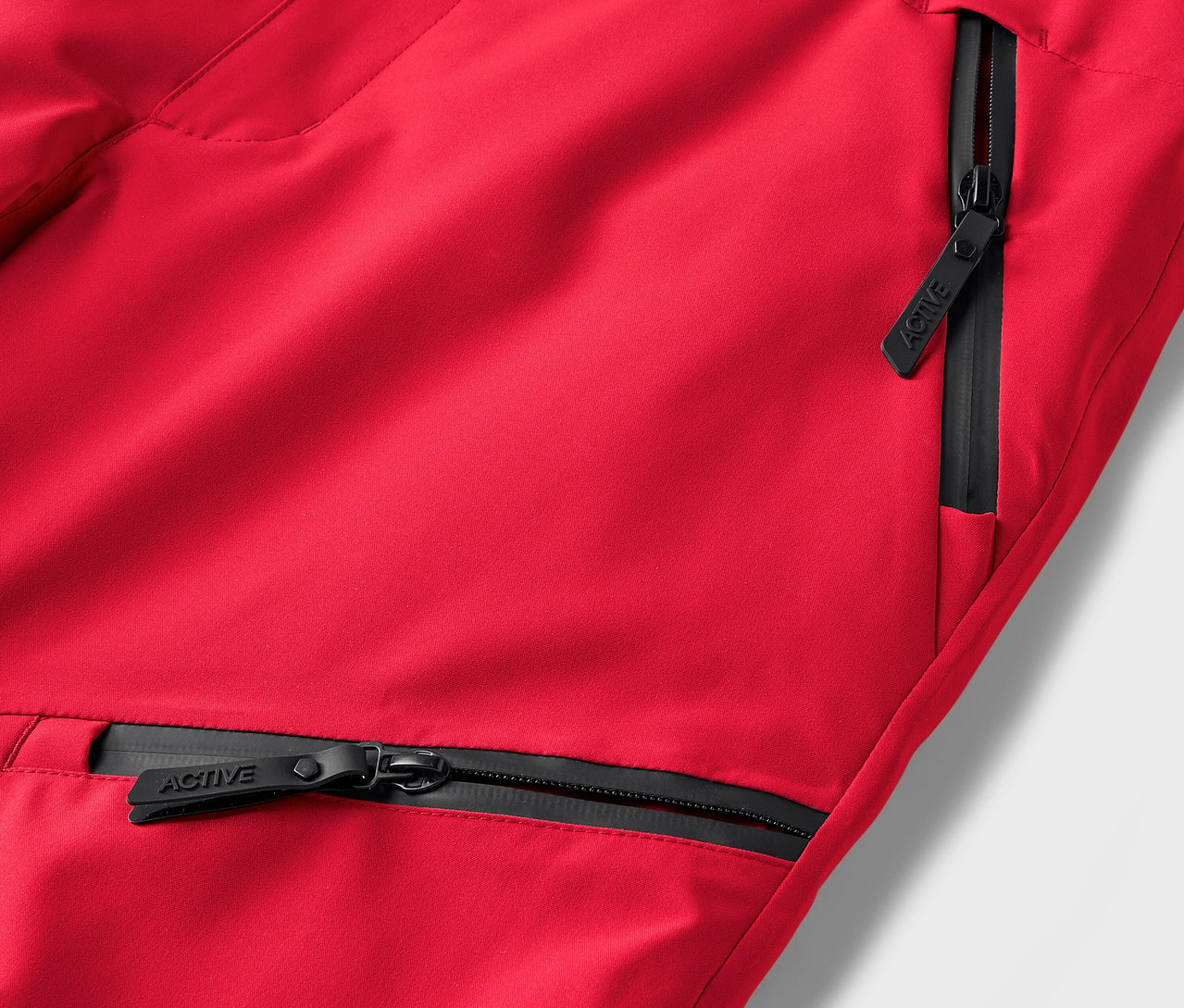 Detail červených nohavíc s čiernymi zipsami vreciek.