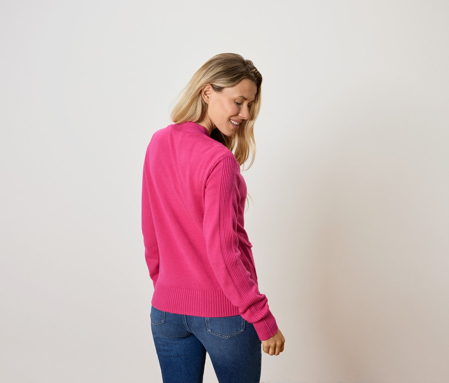 Žena sa pozerá dole a má na sebe ružový sveter a džínsy.