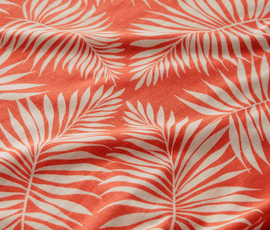 Detailný záber na vzorované blúzkové tričko s motívom bielych palmových listov na koralovom pozadí.