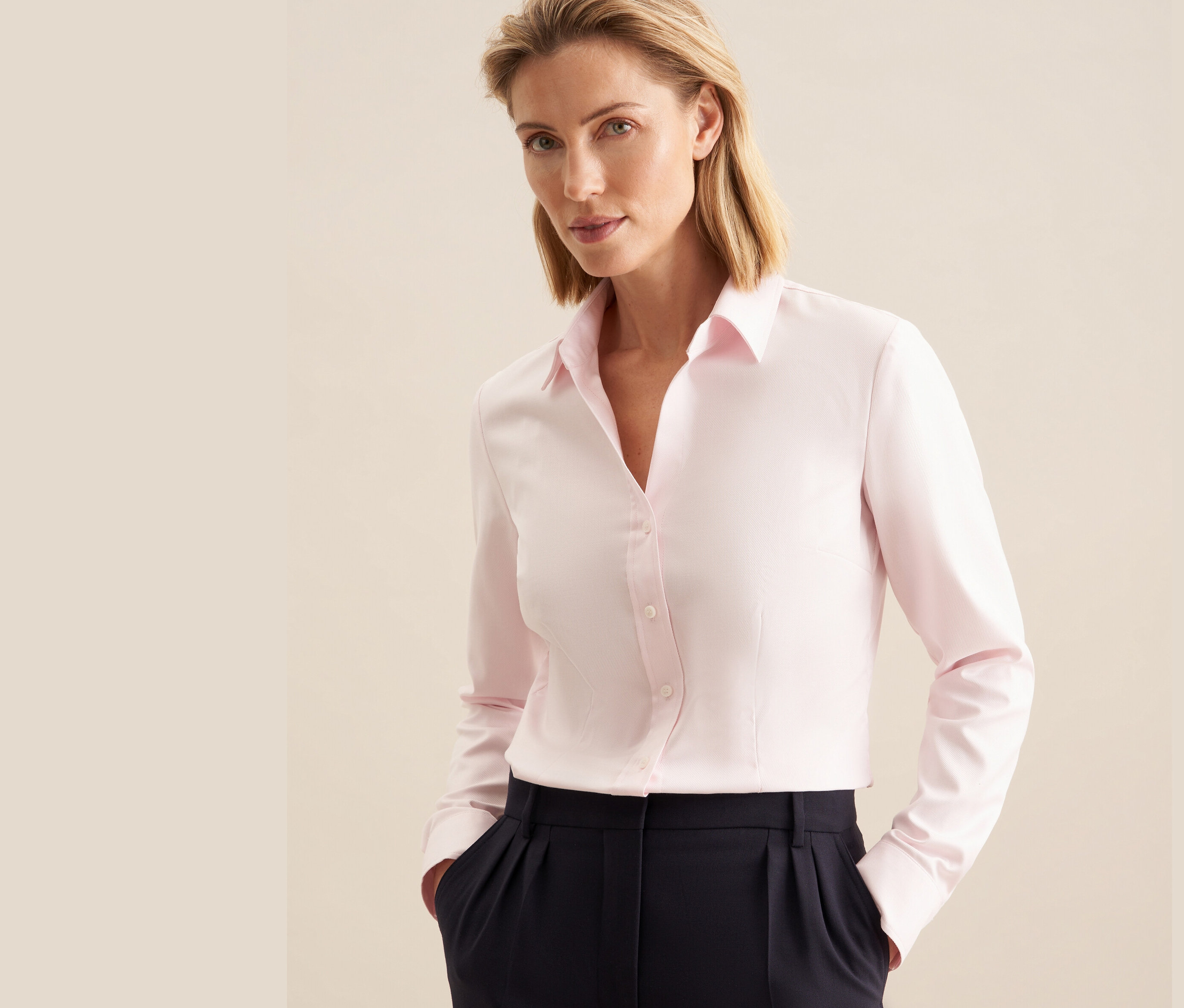 Žena má na sebe ružovú keprovú blúzku Seidensticker a tmavomodré nohavice.