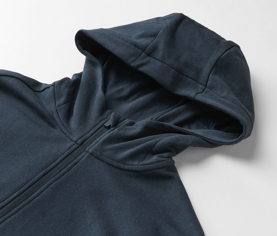 Detail modrej mikiny s kapucňou na zips na bielom pozadí.