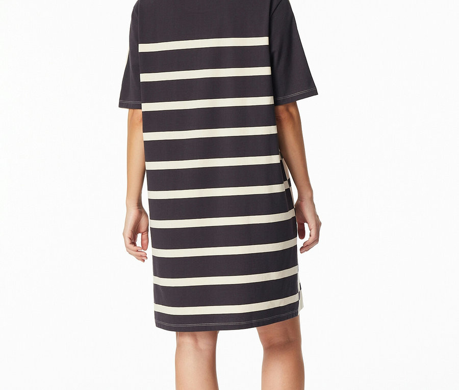 Žena stojí chrbtom k fotoaparátu a má na sebe tmavosivú nočnú košeľu SCHIESSER s krémovými vodorovnými pruhmi.