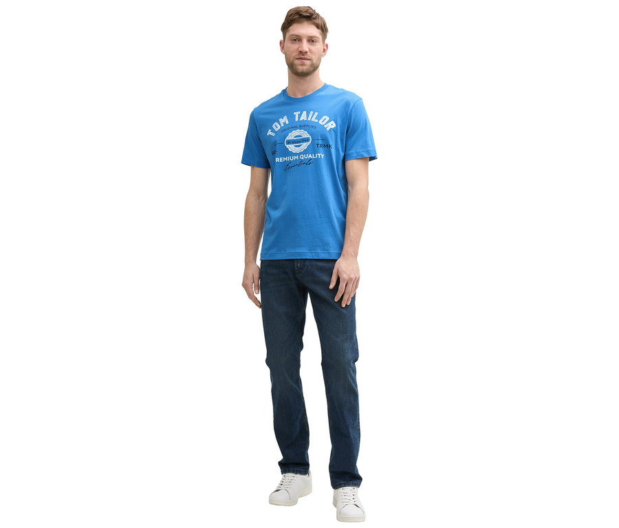 Muž v džínsoch a bielych teniskách má na sebe tričko s logom Tom Tailor vo farbe sapphire blue.