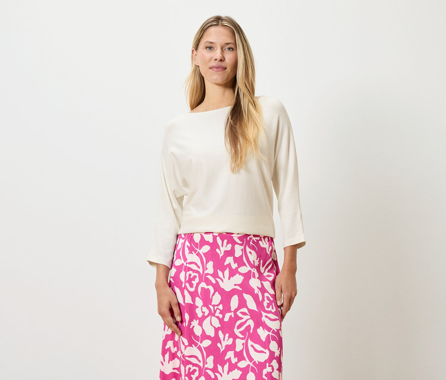 Žena s blond vlasmi má na sebe krémový top a ružovú sukňu s kvetinovou potlačou.